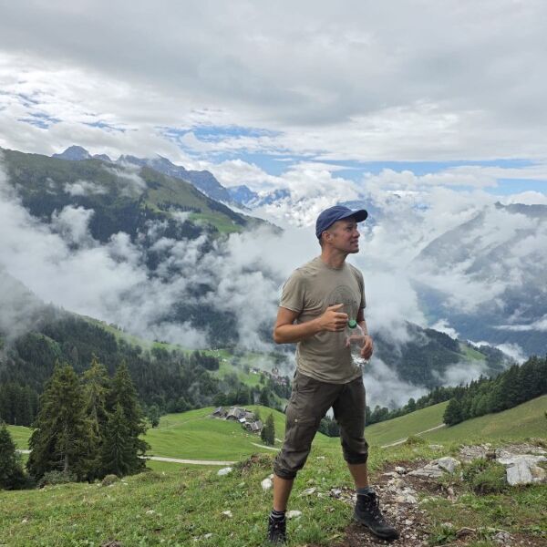 Wanderleiter auf einer Bergwiese vor wolkenverhangenen Gipfeln.