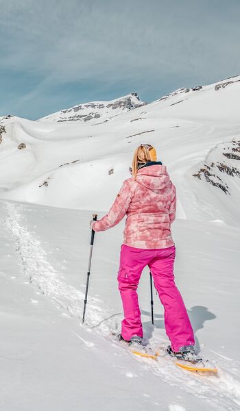 A snowshoer following her trail through the deep snow on the Gemmi Pass towards snowy rocky ridges