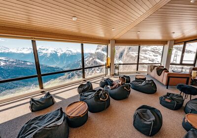 Salle de séminaire pour événements d’entreprise, avec poufs et baies vitrées face aux Alpes valaisannes enneigées