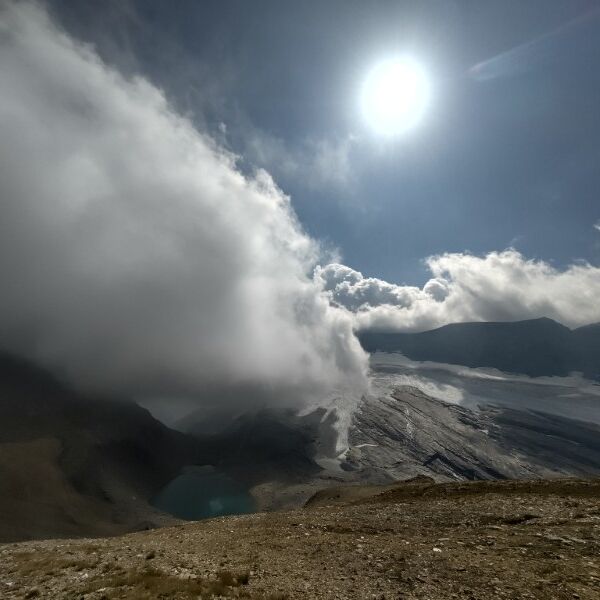 Dichte Wolken ziehen über einen Berggrat, darüber scheint die Sonne.